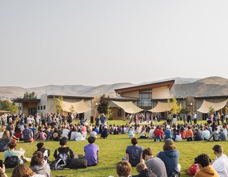 large group sits on a lawn and listens to a speaker